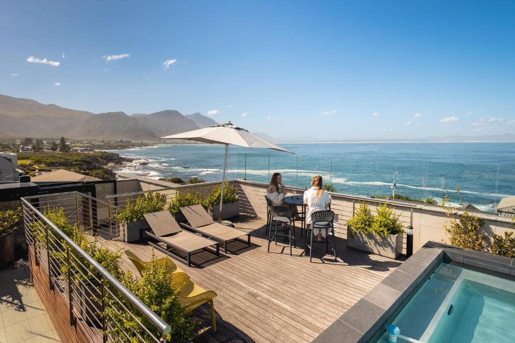 two women sitting at a table on a balcony with the ocean at Hermanus Waterfront Apartments in Hermanus