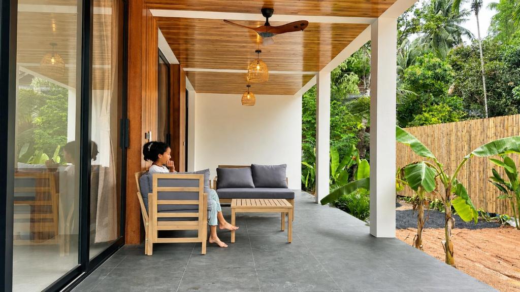 a woman sitting at a table on the porch of a house at Maprao Tropical Home in Ko Phangan