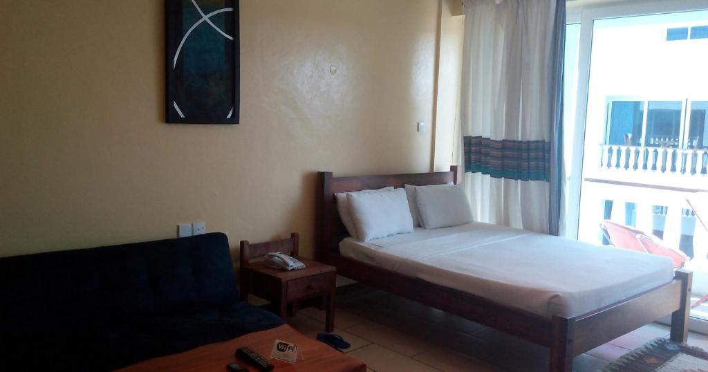 a bedroom with a bed and a couch and a window at Sunny Beachfront Studio in Mombasa