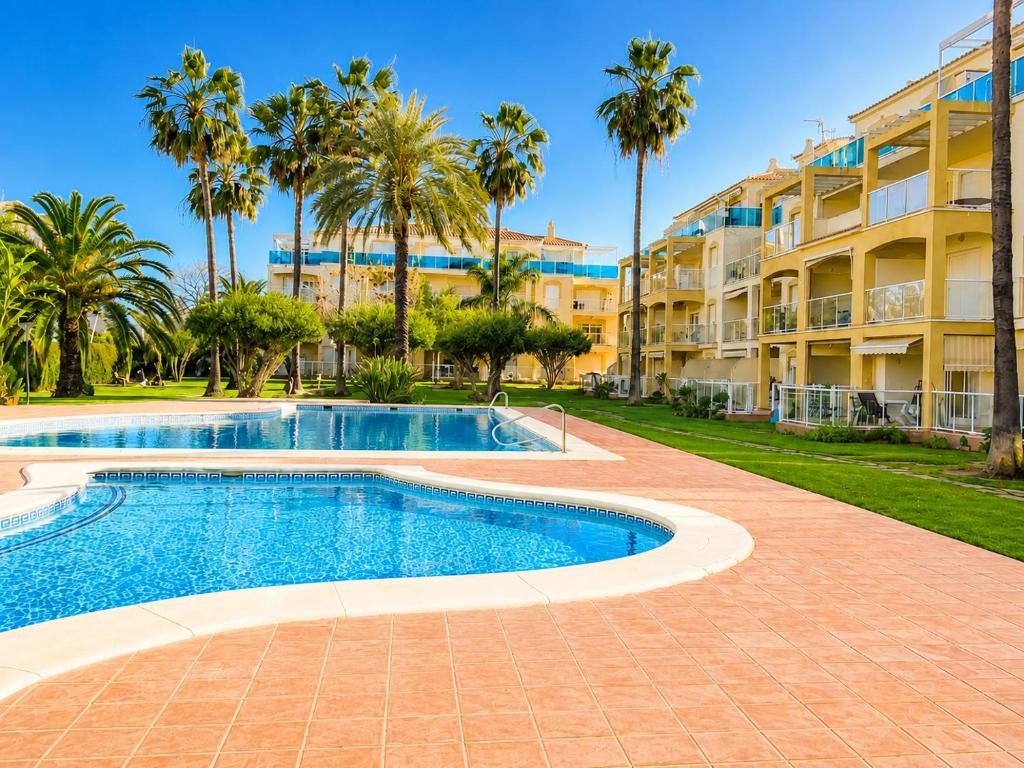 a swimming pool with palm trees and a building at Dénia Palm Garden Apartment Pool & Parking in Denia