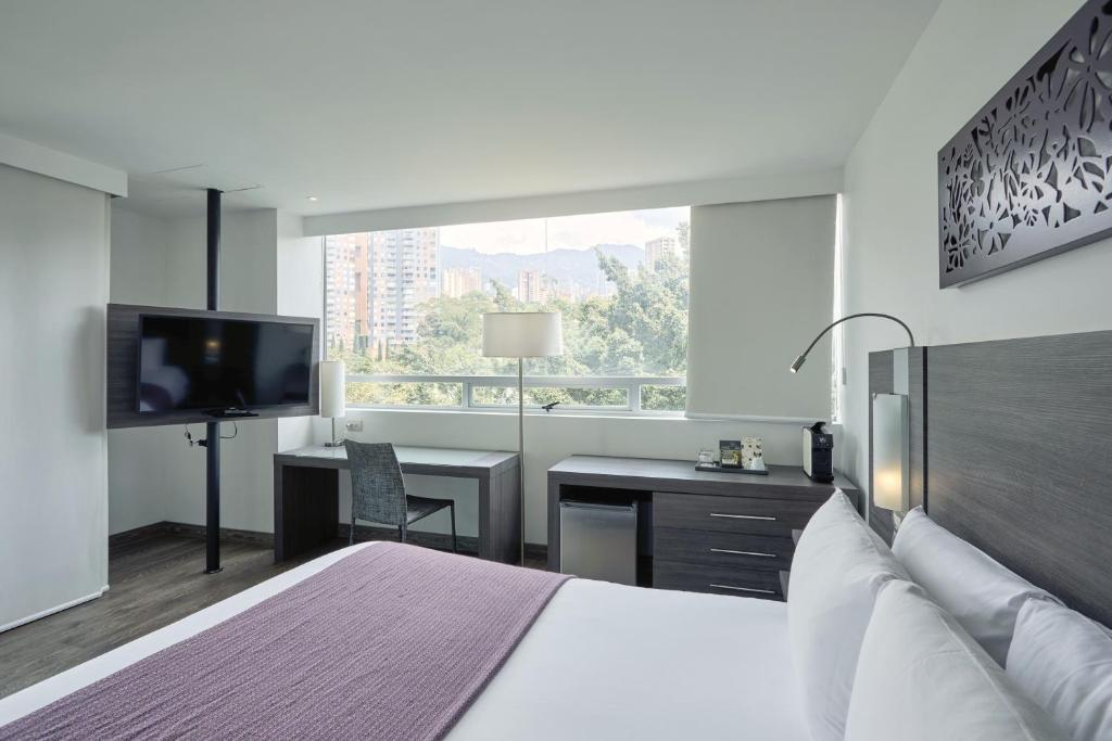 a bedroom with a bed and a desk and a television at Hotel bh El Poblado in Medellín