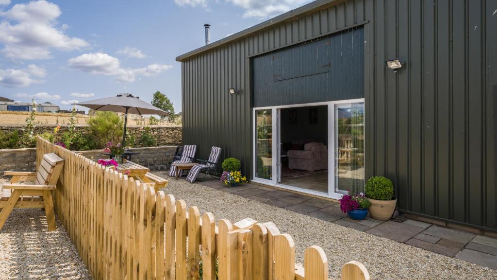 a green house with a wooden fence and chairs at Roe Barn in Sherston