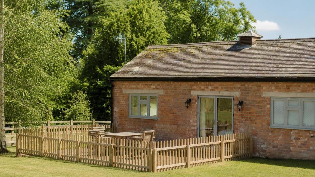a brick house with a wooden fence in front of it at Paddock Cottage in Winchcombe