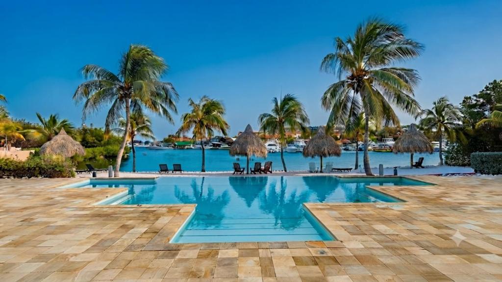 a pool at the resort with palm trees at Luxury Ocean View Apartment, Private Beach, Infinity Pool, near Jan Thiel C3 in Willemstad
