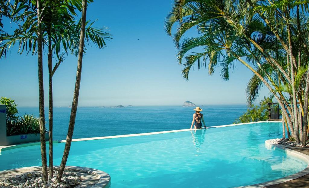 a person standing in a swimming pool next to the ocean at La Suite by Dussol in Rio de Janeiro