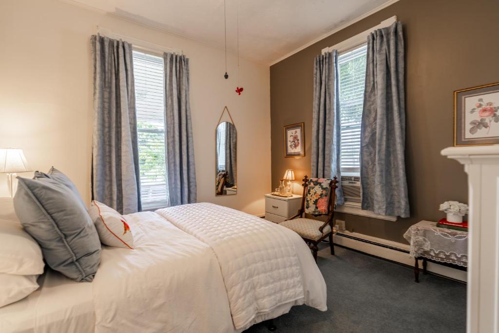 a bedroom with a bed and a chair and windows at Victorian Inn Bed And Breakfast in Marblehead