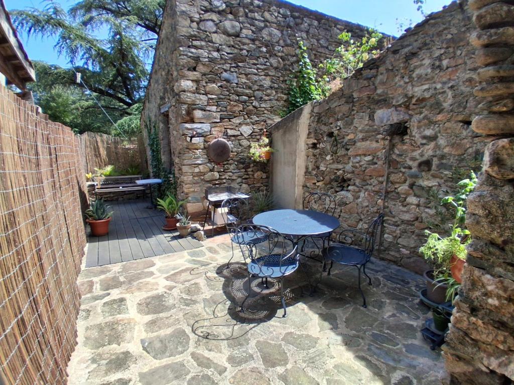 a patio with a table and chairs in a stone wall at Les volets bleus in Prémian