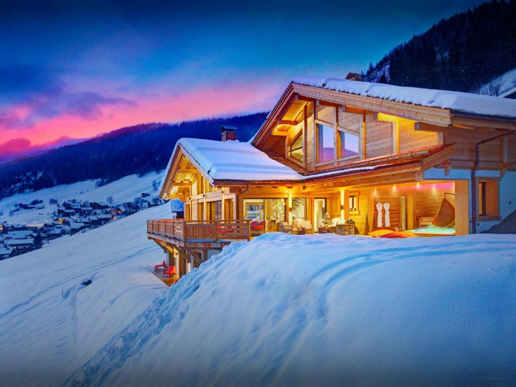a house in the snow at dusk with the sun setting at Chalet Alti - OVO Network in Le Grand-Bornand