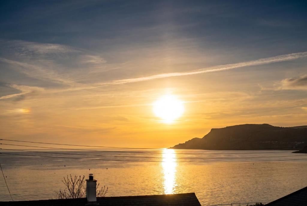 a sunset over a body of water with a lighthouse at Cushendall Coastal Accommodation, Glens of Antrim - Beach & Mountain Access in Cushendall
