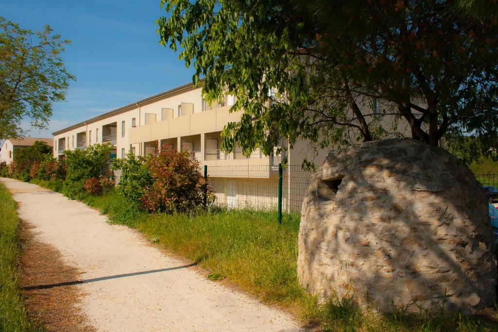 una roccia sul ciglio di una strada accanto a un edificio di La Résidence Des Oliviers a Bagnols-sur-Cèze