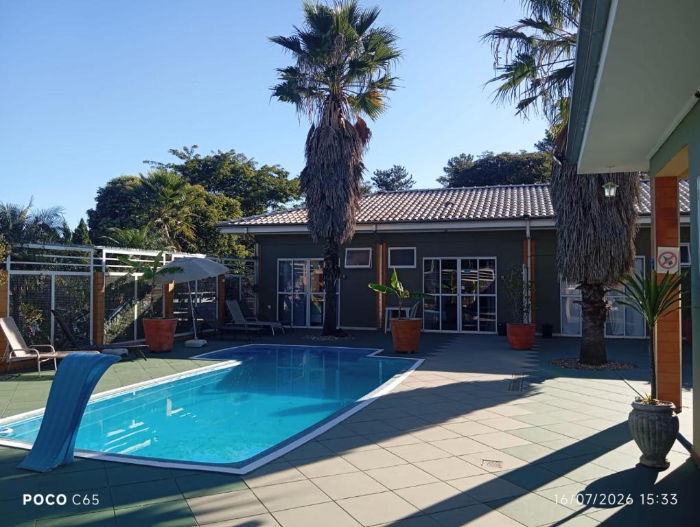 a swimming pool with palm trees and a house at Suits Recanto do Sabiá in Brotas