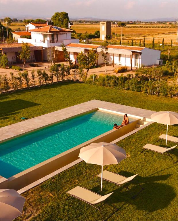 a person sitting on a lawn next to a pool with umbrellas at Radicata Tuscany Relais in Albinia