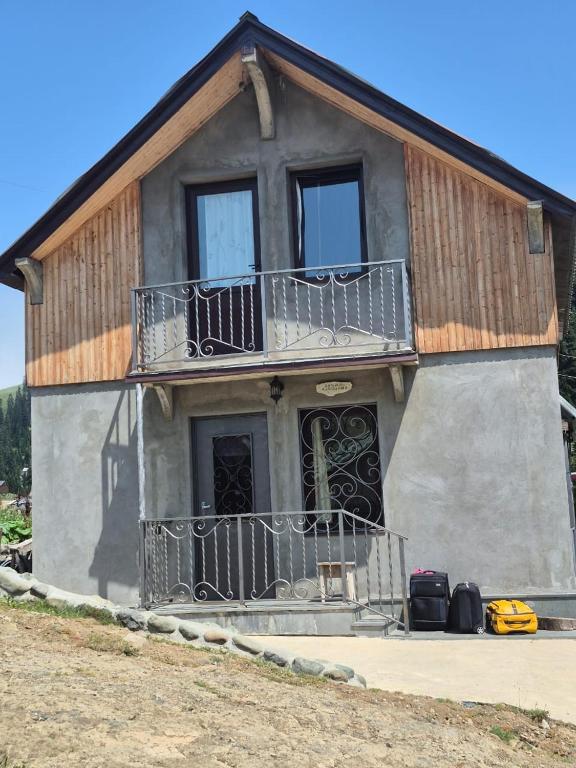 a house with a balcony and luggage in front of it at Cozy Mountain Chalet Bakhmaro in Chʼkhakoura
