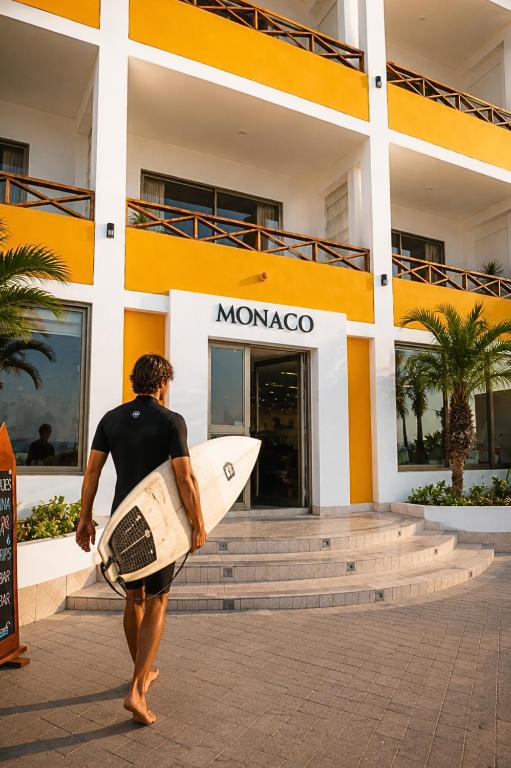 a man carrying a surfboard in front of a building at Monaco Chicama Beach in Puerto Chicama