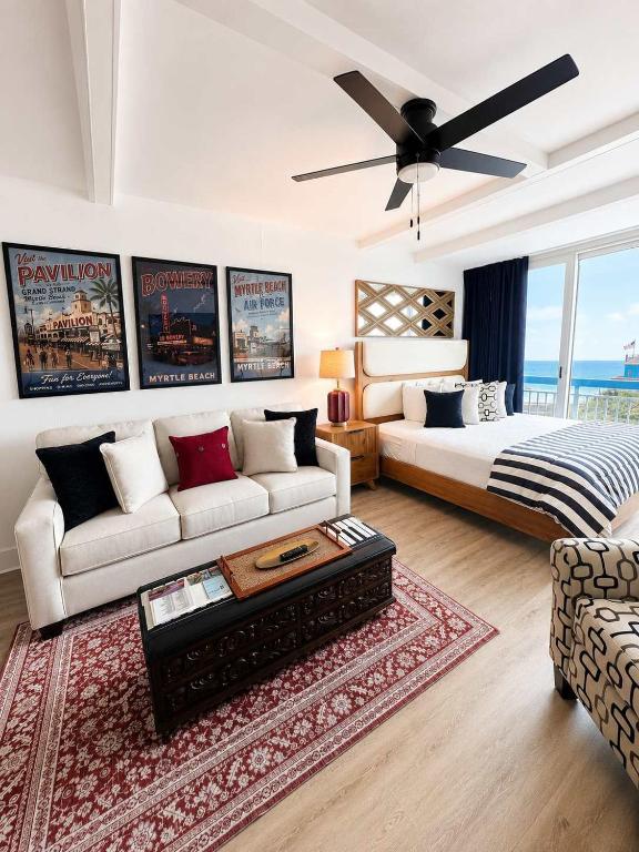 a living room with a couch and a bed and a ceiling fan at Boardwalk Noir - Oceanfront Studio Yachtsman 404 in Myrtle Beach