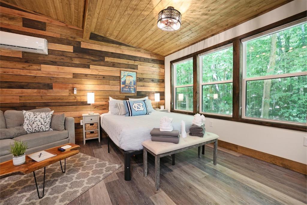 a bedroom with a bed and a couch and windows at Tiny Tarheel Cozy Retreat Near UNC-Tiny House in Chapel Hill