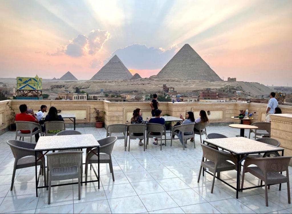 people sitting at tables on a roof with pyramids in the background at Royal Moses Pyramids View Hotel in Cairo