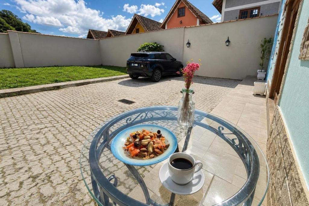a plate of food on a glass table with a cup of coffee at Chalé Charmoso na Serra de Penedo in Penedo