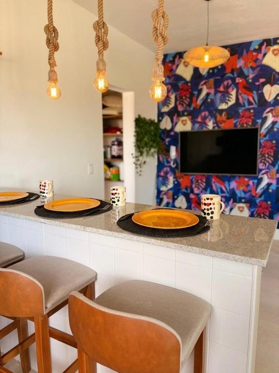 a kitchen with a counter with orange plates and chairs at Apartamento Centro Bertioga Casal e Família - Ar Condicionado - Praia da Enseada in Bertioga