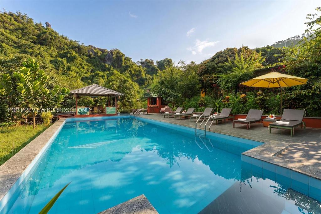 a pool with chairs and umbrellas next to a mountain at Catba Papillon Garden Bungalows & Resort in Cat Ba