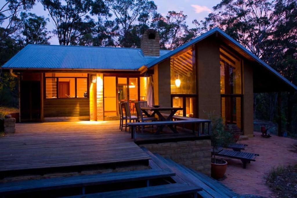 a house with a wooden deck with a picnic table at Corymbia Cottage Brokes Secluded Escape for max 4 in Broke