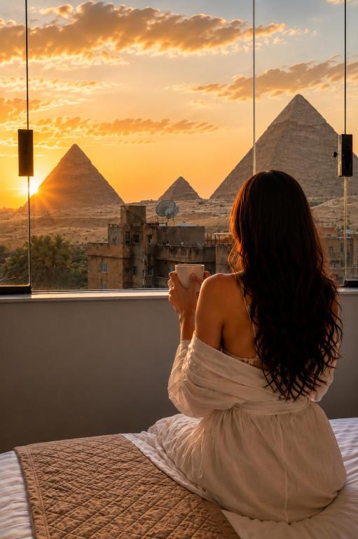 a woman sitting on a bed looking out a window at the pyramids at Royal Aida Pyramids View INN in Cairo