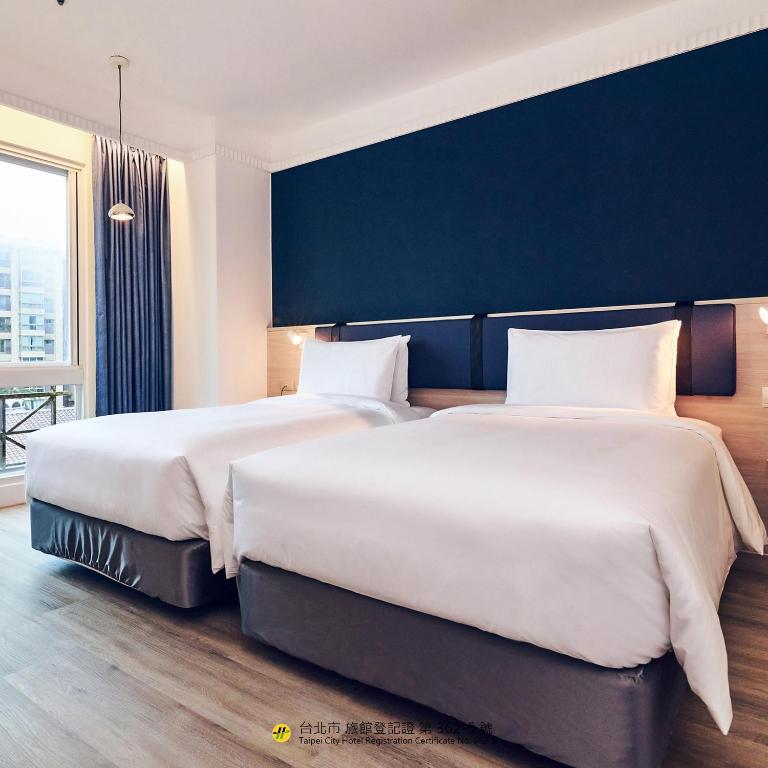 two beds in a hotel room with a blue wall at CHECK inn Select Taipei Nangang in Taipei