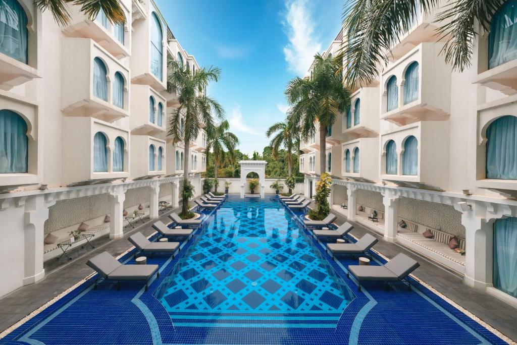 an image of a swimming pool with lounge chairs and palm trees at Sarai and Wander Resort in Siem Reap