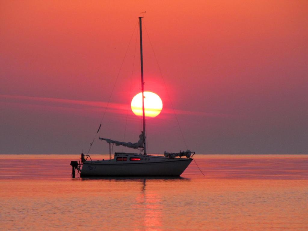 un barco en el agua con una puesta de sol en el fondo en Beachside Guest House Strautini, en Plieņciems
