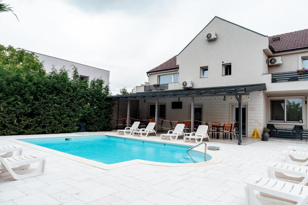 a swimming pool with white chairs and a house at XO Residence in Arad