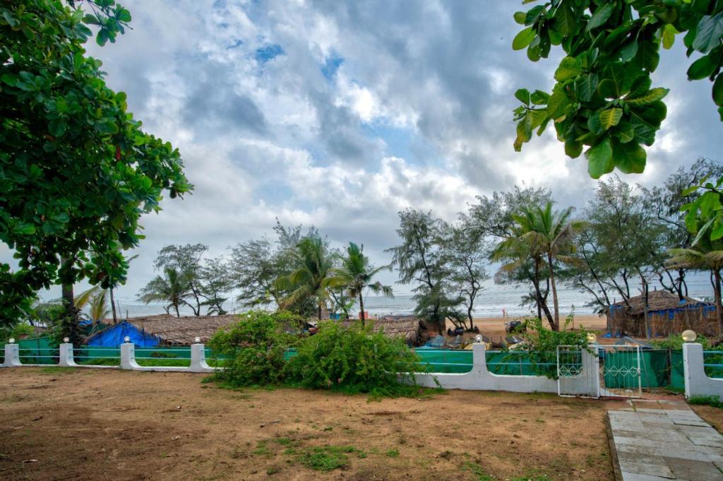 a fence in front of a beach with palm trees at Baga Wave Edge Cottages in Baga