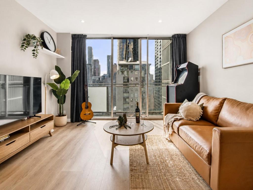 a living room with a couch and a table and a large window at Elevated CBD Retreat - Views & Pool & Sauna! in Melbourne