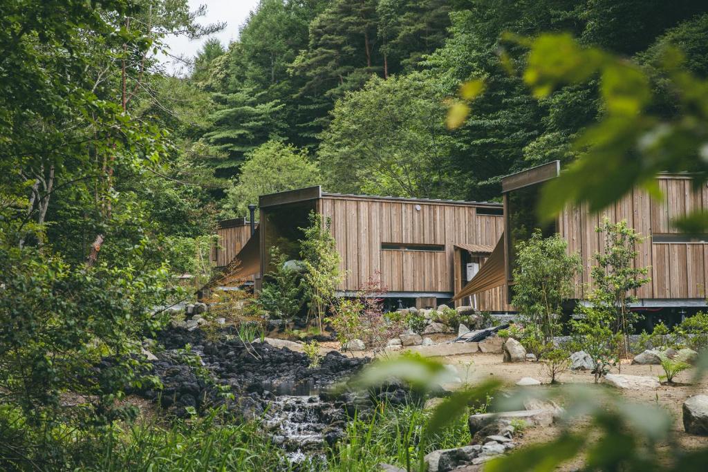 a wooden house in a forest with a stream at Earthboat Ueda Onsen in Nagano