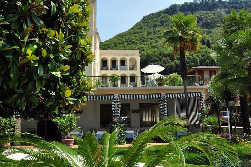 a building with palm trees and a mountain in the background at Hotel Terminus in Garda