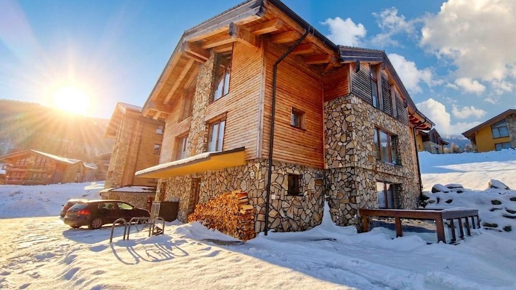 a log cabin in the snow with the sun behind it at Jasna Chalet - Chopok view Apartment with sauna and whirlpool bathtub in Belá