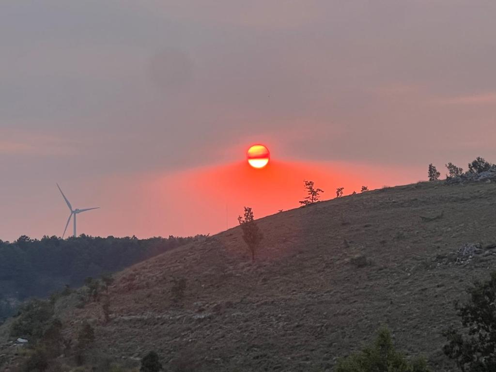 a sun setting over a hill with a wind turbine at El Pecu Casa Rural Starfamiliar in Bustillo del Páramo