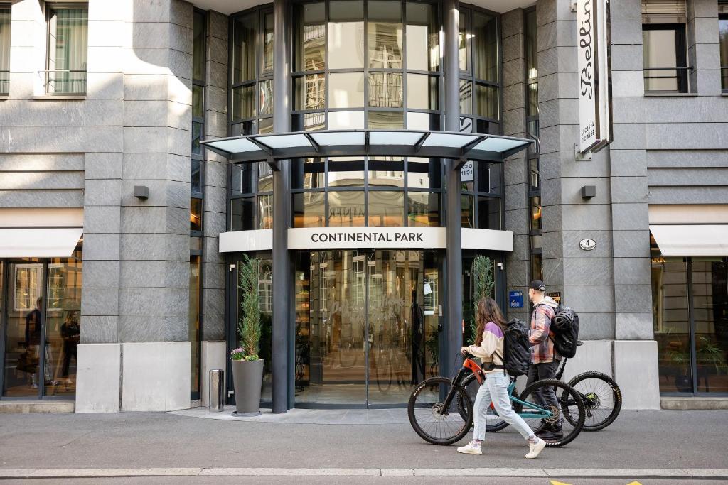 two people walking their bikes in front of a building at Hotel Continental Park in Lucerne