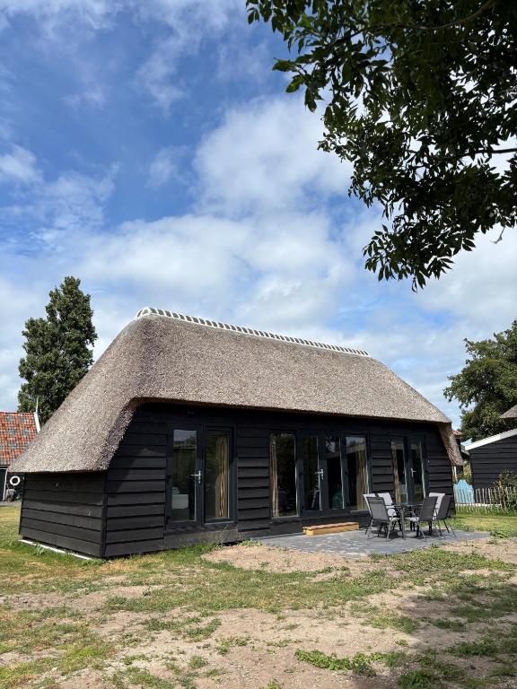 a small house with a thatched roof and chairs at Lodge Wieringen in Hippolytushoef