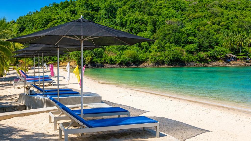 a row of beach chairs with an umbrella on a beach at MG Chateau Resort in El Nido