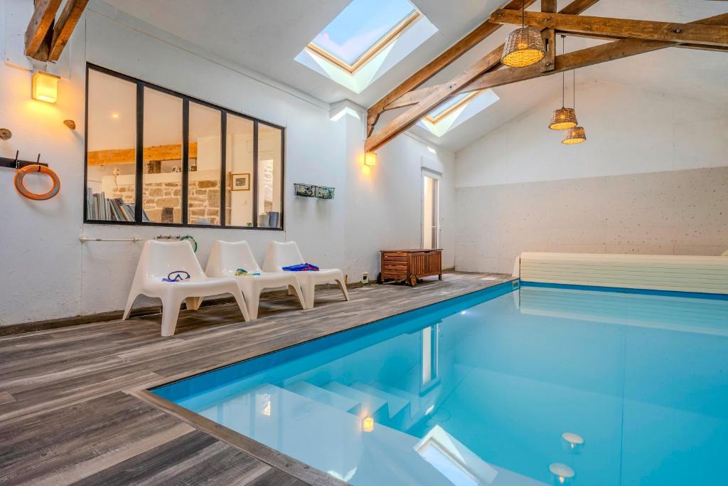 a swimming pool with two chairs and a table at Villa Léonie - piscine intérieure in Kerlouan