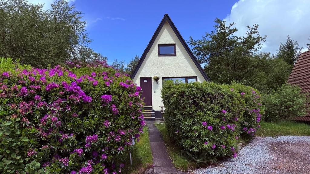 a small house with purple flowers in front of it at 1 Bedroom Cabin with Mountain & Loch Views - Quiet Location between Glencoe & Ben Nevis in Corran