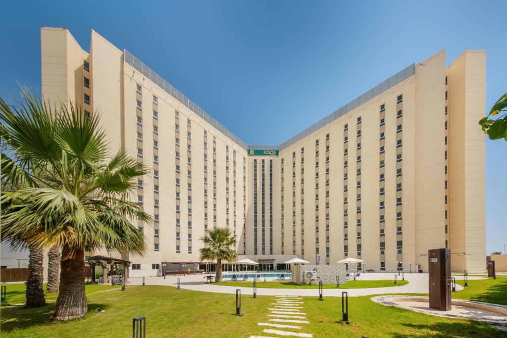 a large building with a palm tree in front of it at Acacia Hotel Ras Al Khaimah by AMR in Ras al Khaimah