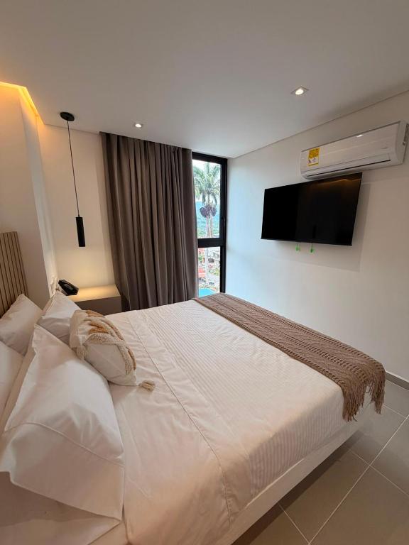 a bedroom with a large white bed with a flat screen tv at Hotel Palmaris Urban Villeta in Villeta