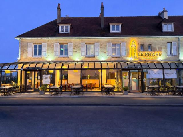 a large building with tables and chairs in front of it at Hôtel Le Phare in Ouistreham