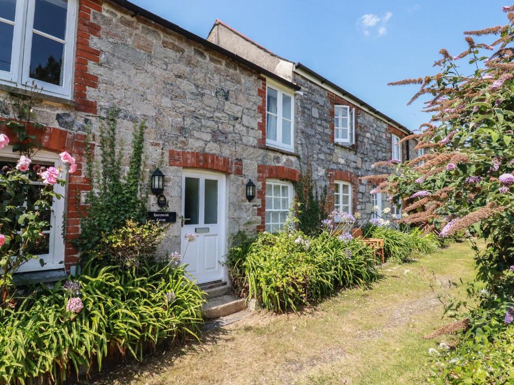 an old stone house with a white door and flowers at Honeysuckle Cottage in St Austell