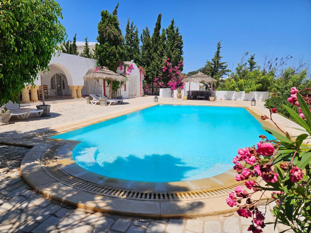 a large swimming pool in a yard with flowers at Dar El kharrouba in Hammamet Nord
