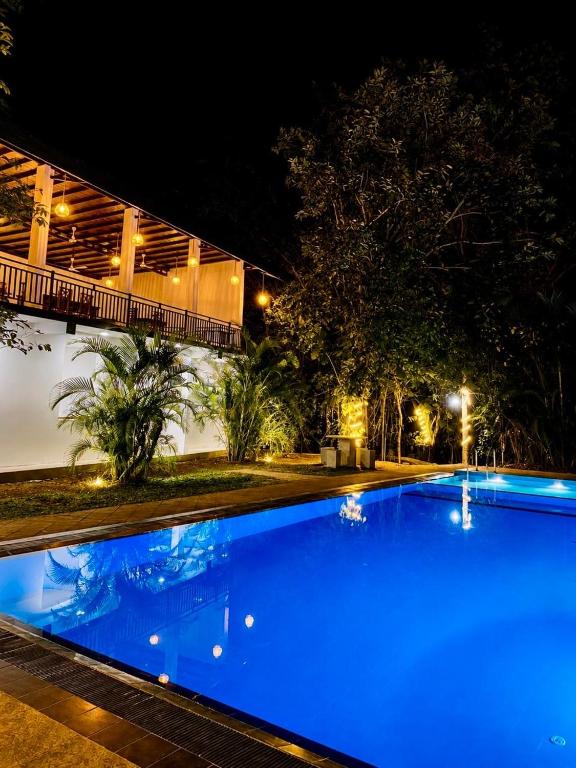 a blue swimming pool in front of a building at night at Dudley Nature Resort in Habarana