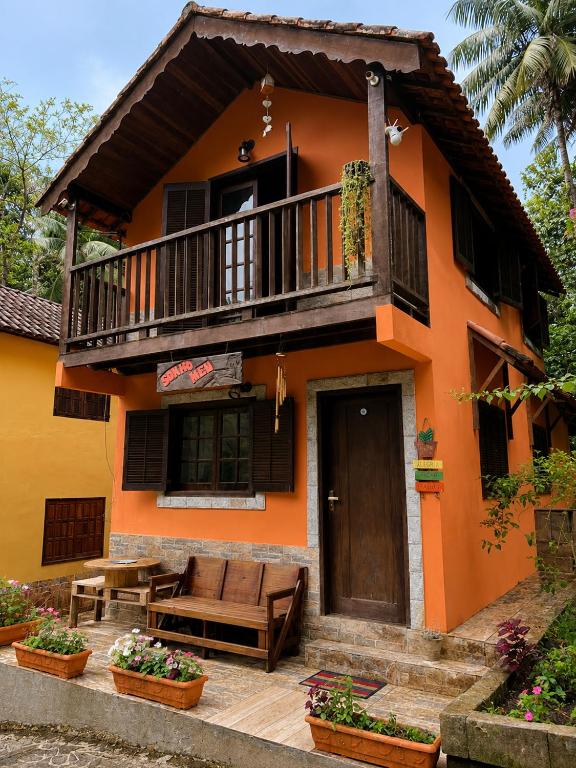 an orange house with a balcony and a patio at Chalé Sonho Meu Penedo in Itatiaia