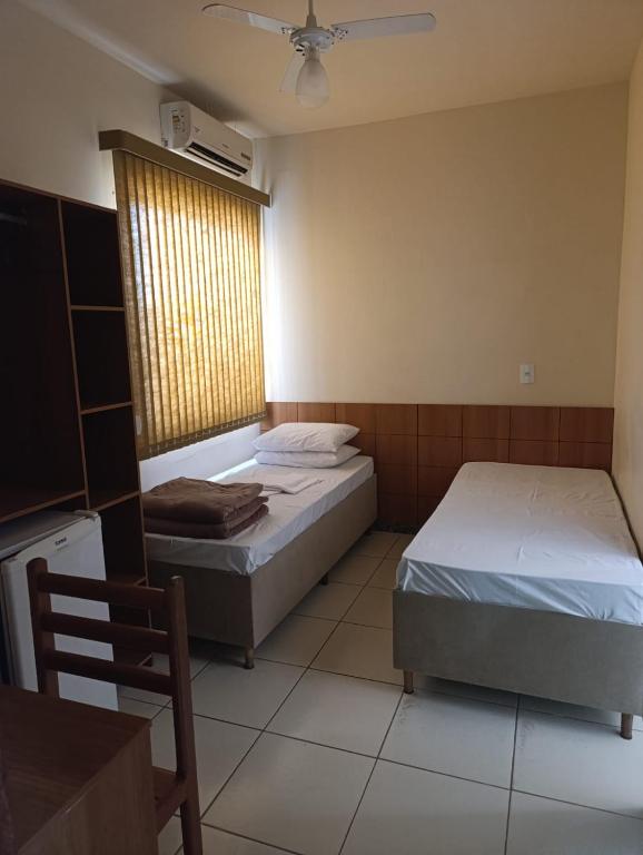 a bedroom with two beds and a window with a fan at Ubaense Suites in Ubá