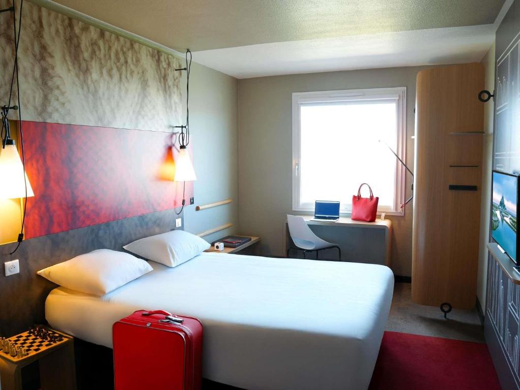 a hotel room with a white bed and a red suitcase at ibis Caen Porte De Bretagne in Bretteville-sur-Odon